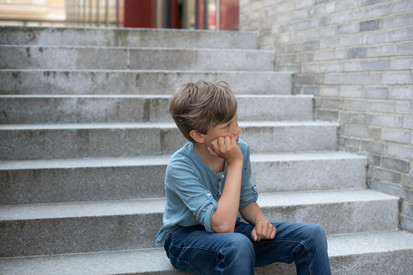 Über uns Ein kleiner Junge sitzt traurig auf einer Treppe