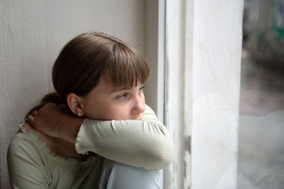 Pakt gegen sexualisierte Gewalt Eine Mädchen sitzt am Fenster und Blickt traurig nach draußen.