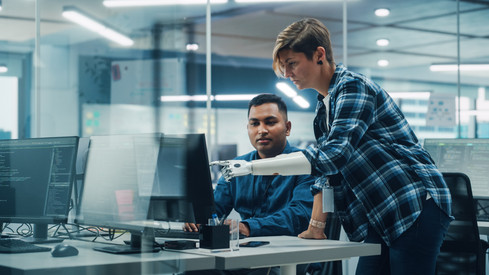 Projektmanagerin mit Armprothese spricht mit indischem Spezialisten bei der Arbeit am Desktop-Computer