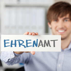 Ehrenamtliches Engagement Symbolbild: Mann hält Schild hoch mit Schriftzug "EHRENAMT"