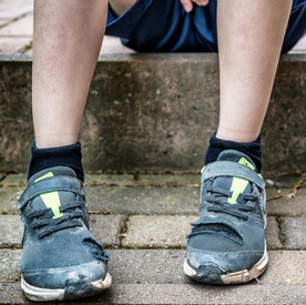 Unkenntliches Kind sitzt mit kaputten Schuhen auf Gehweg