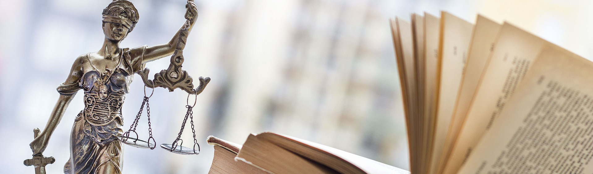 Figur der Justitia neben einem aufgeschlagen Buch- Symbolbild für Gesetzgebung
