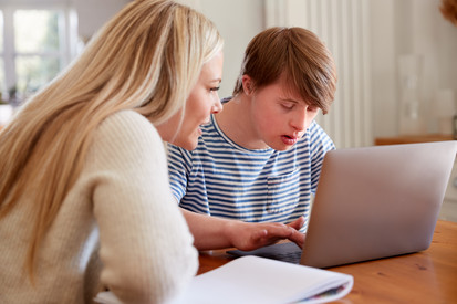 Junger Mann mit Down Syndrom arbeitet gemeinsam mit einer Tutorin am Laptop.