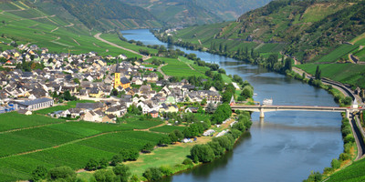 Ein Bild eines Dorfes, das an einem Fluss liegt. Eine Brücke verbindet das Dorf mit der anderen Uferseite.