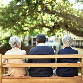 Drei Senioren sitzen gemeinsam auf einer Parkbank