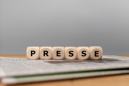Würfel bilden das Wort Presse auf einer Zeitung vor grauem Hintergrund