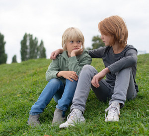 Symbolbild: Zwei traurige Kinder sitzen auf einer Wiese